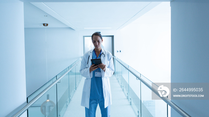 Female surgeon using digital tablet in the corridor of hospital