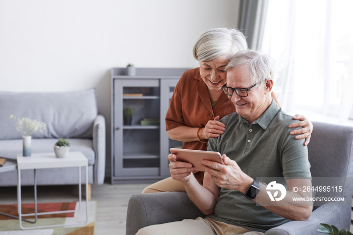 Portrait of happy senior couple using digital tablet together in minimal home interior, copy space