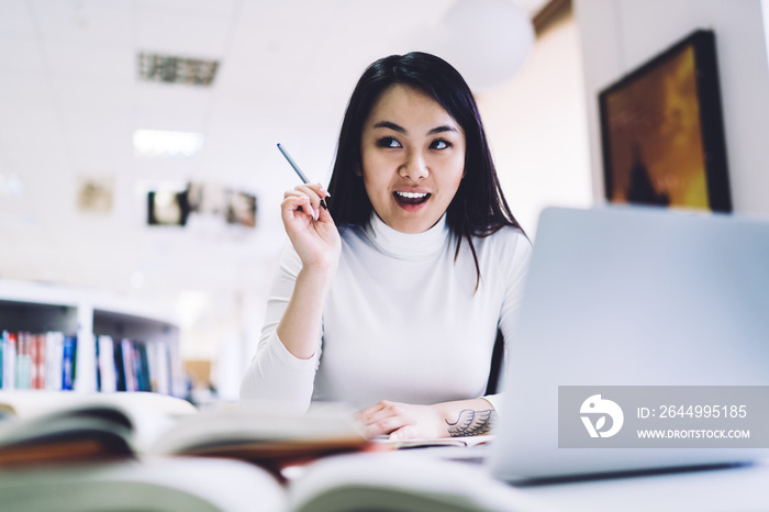 Adult ethnic businesswoman developing strategy while sitting at laptop with notepad and books in office