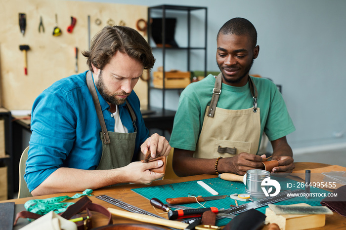 Portrait of modern male artisan teaching young apprentice in leatherworkers workshop, copy space