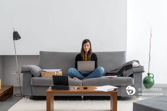 Young woman with laptop telecommuting on the sofa at her home