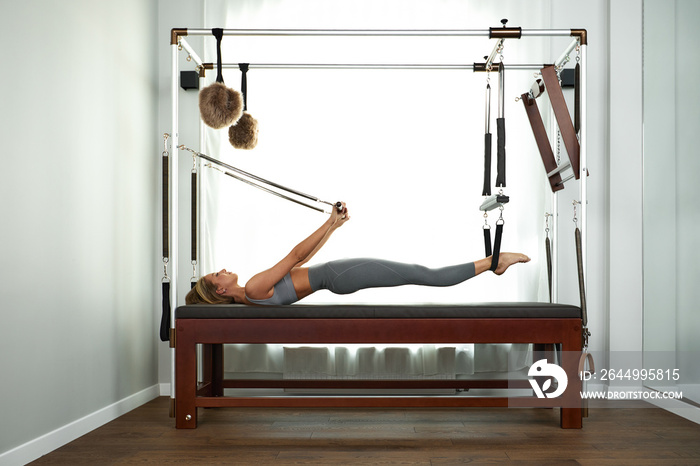 The instructor does exercises on the reformer, a beautiful girl trains on the modern reformer simulator to work out deep muscles, the modernized reformer equipment for Pilates and yoga.