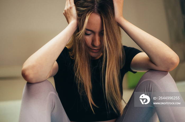 Young attractive tired woman sitting on a fitness mat after training at home