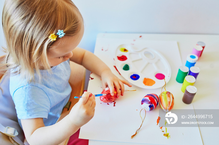 Adorable little girl painting eggs for Easter