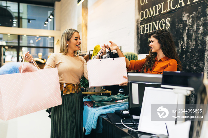 Beautiful young blond woman paying her new clothes buyed in expensive boutique with credit card.