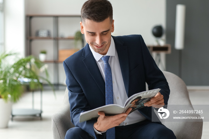 Young man in stylish suit reading magazine at home