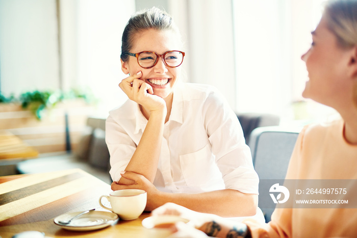 Friendly young businesswomen laughing while interacting by cup of tea at leisure