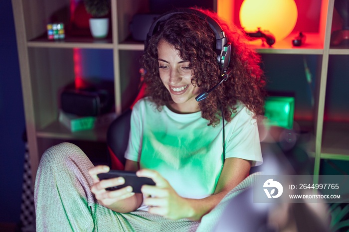 Young beautiful hispanic woman streamer playing video game using smartphone at gaming room