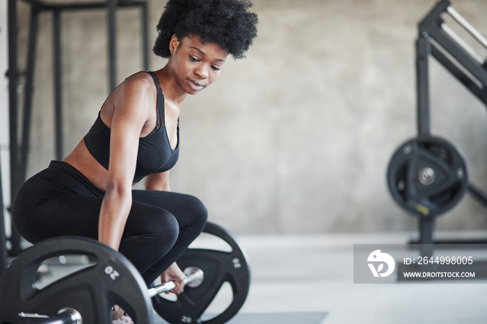 Lifting exercises. African american woman with curly hair and in sportive clothes have fitness day in the gym