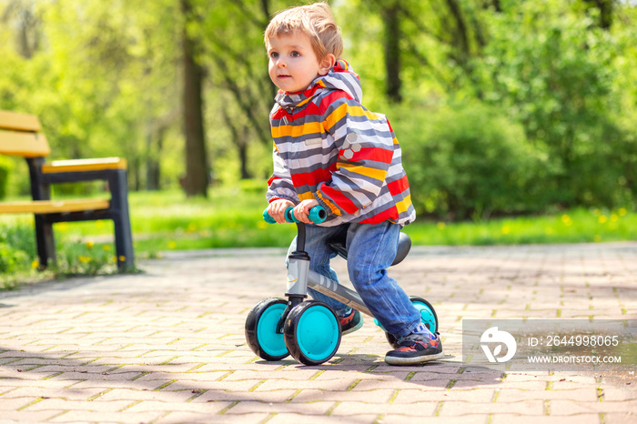 Active blond boy riding balance bike or run bike outdoor park