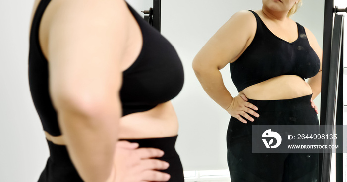 Chubby woman standing and looking at her stomach in a mirror.