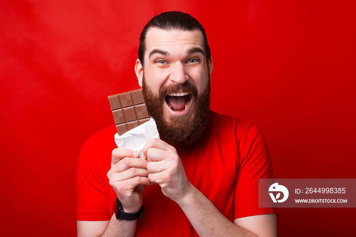 A very excited man is eating a chocolate in front of camera looking at it .