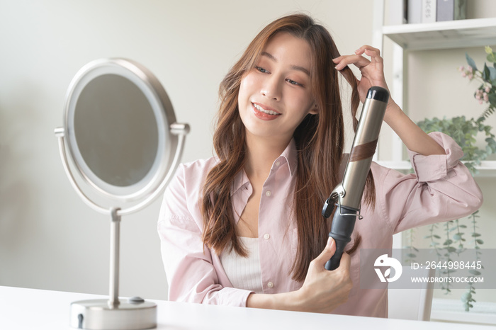 women hairdo makeup routine, Young woman looking at the mirror and using iron hair curling curly long hair at home.