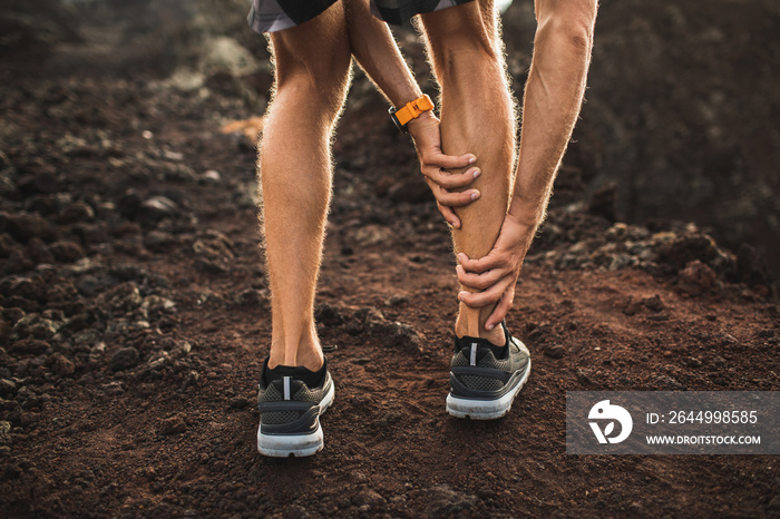 Male runner holding injured calf muscle and suffering with pain. Sprain ligament while running outdoors. View from the back close-up.