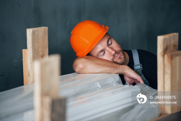 Sleeping on a job. Taking a break. Industrial worker indoors in factory. Young technician with orange hard hat