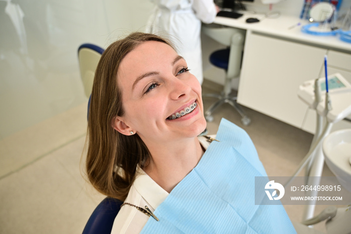 The smile of a young and beautiful girl with braces on her white teeth. Straightening of crooked teeth with the help of a bracket system. Malocclusion. Dental care. Smooth teeth and a beautiful smile