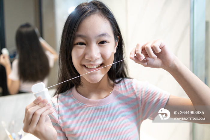 Happy smiling asian student girl flossing her teeth,clean her healthy teeth in the morning,beautiful woman brushing with dental floss in the bathroom, teeth care,oral hygiene,dental health concept