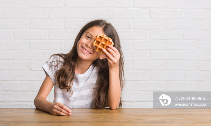 Young hispanic kid sitting on the table eating waffle with a happy face standing and smiling with a confident smile showing teeth