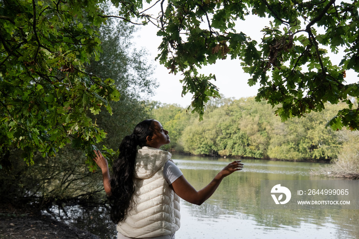 Rear view of woman standing by river with arms raised