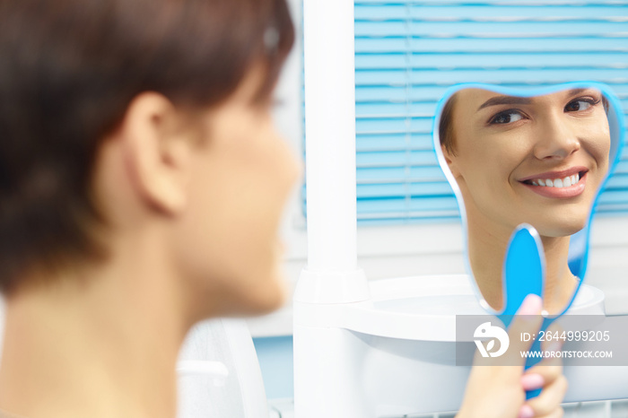 Young female patient visiting dentist office.Beautiful smiling woman with healthy straight white teeth looking at mirror.Dental clinic.Stomatology