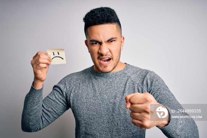 Handsome man holding reminder paper with sad emotion face emoji over white background annoyed and frustrated shouting with anger, crazy and yelling with raised hand, anger concept