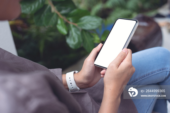 Mockup image of woman sitting cross legged using white mobile phone with blank black screen