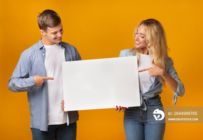 Millennial couple holding blank advertising board and pointing on it