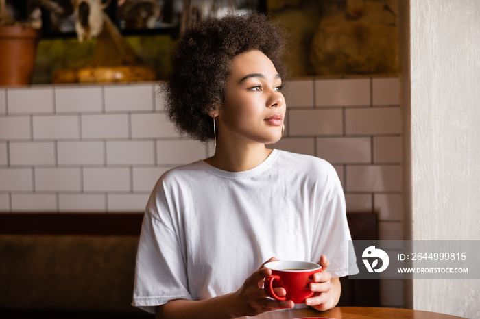 thoughtful african american woman in white t-shirt holding cup