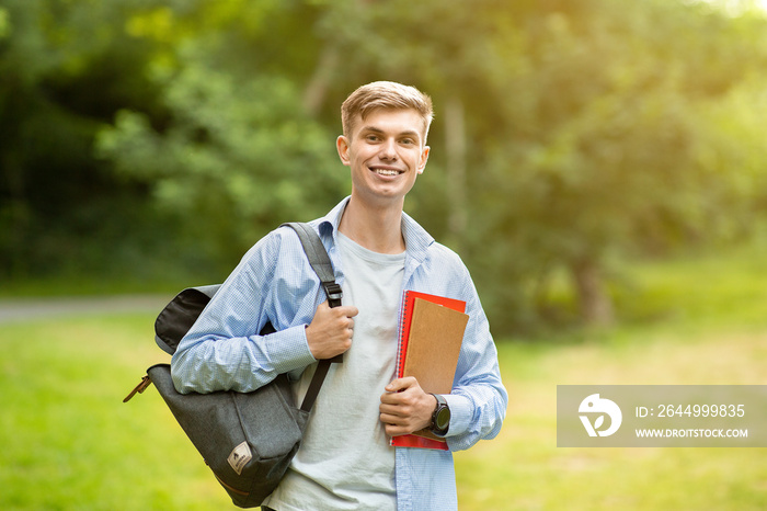 Portrait Of Handsome University Student Guy With Backpack And Workbooks Posing Outdoors