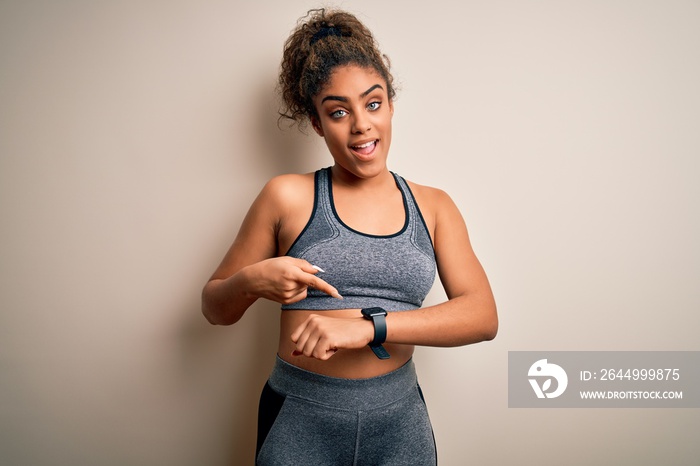 Young african american sportswoman doing sport wearing sportswear over white background In hurry pointing to watch time, impatience, upset and angry for deadline delay