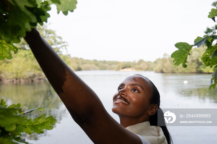 Portrait of smiling woman touching leaves on tree by river