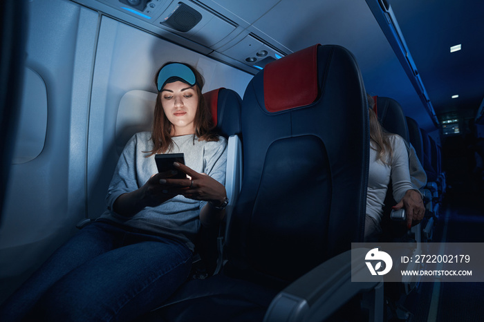 女性在夜间飞行时点击智能手机