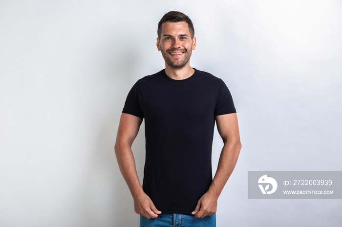 Funny man wearing in black t-shirt standing pulling down a t-shirt smiling and looking at the camera