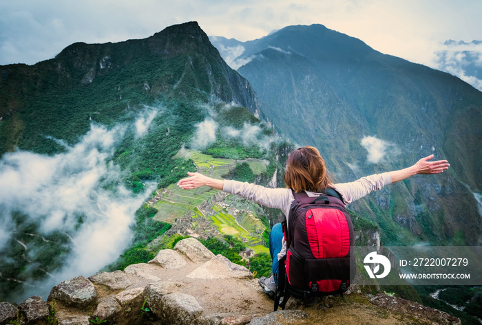 View of girl sitting on the edge of the rock with raised hands and taking pleasure of breathtaking f