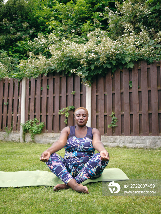 Woman meditatingÊon yoga mat in backyard