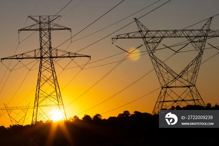 The sun rising behind a pair of towering electricity pylons