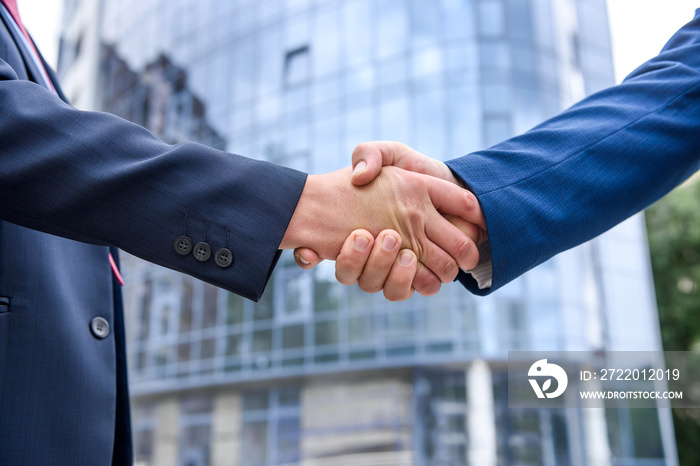 Friends in elegant business suits handshaking outdoors