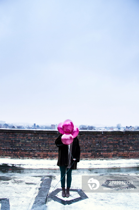 一名女子站在大楼露台上，用粉色气球遮住脸