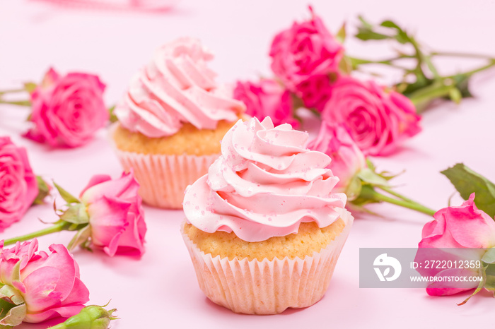 粉红色奶油装饰的纸杯蛋糕，粉红色粉彩背景上的玫瑰。