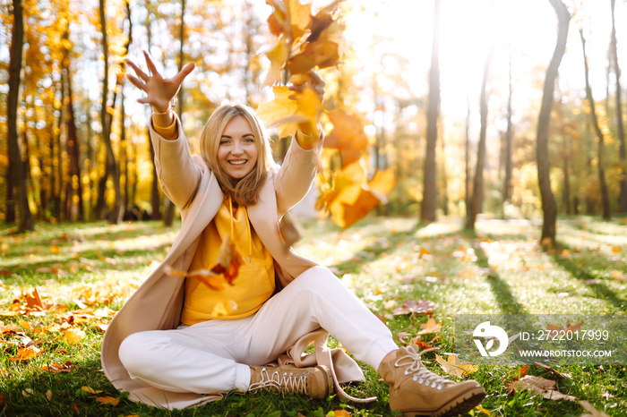 Smiling woman playing with autumn  yellow leaves.  Stylish woman enjoying autumn weather in the park