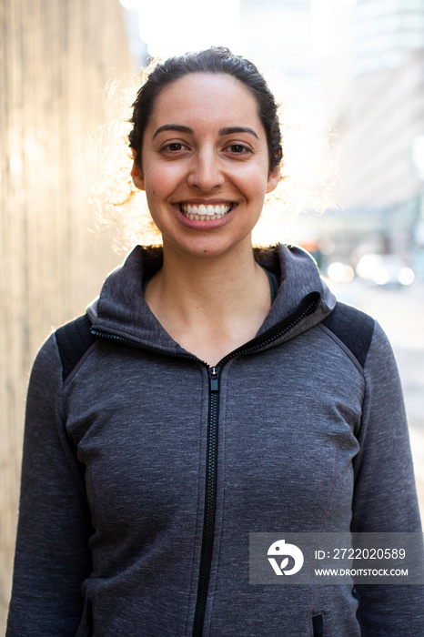 Portrait of smiling confident female athlete standing on sidewalk in city