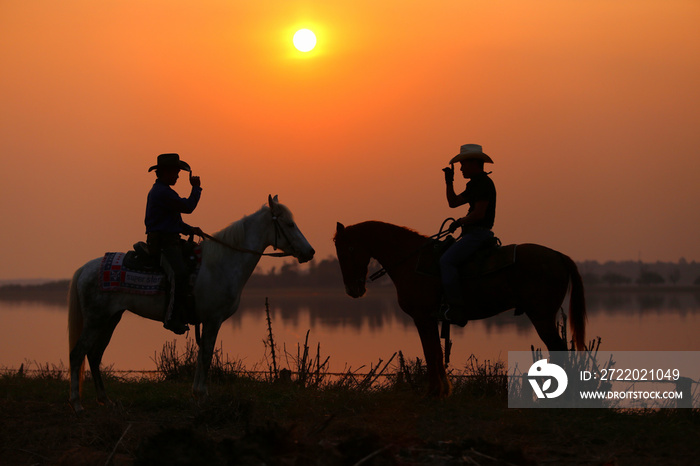 Silhouette Cowboys and friends meet each other on horseback to watch the sunset.