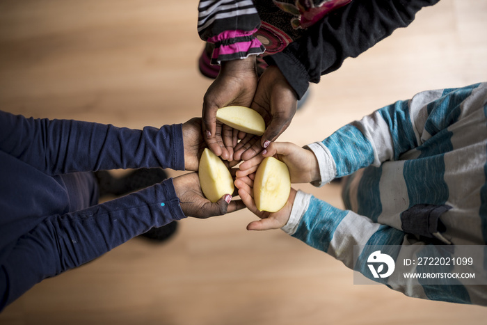 Three kids of mixed races each holding a piece of apple in the p