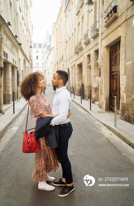 Side view of romantic couple looking at each other while standing on street amidst buildings in city