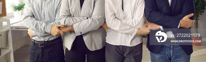 Team of male and female business people standing together in office, holding hands, supporting each 