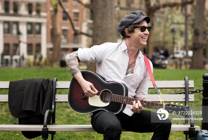 Street musician playing guitar while sitting on bench at park