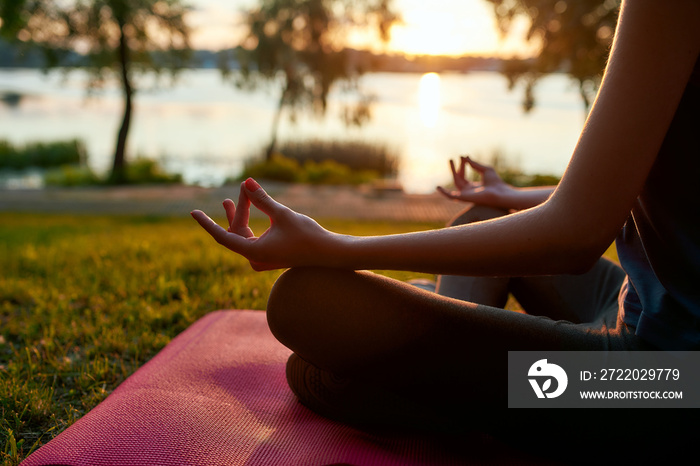 Cropped shot of a woman practicing yoga in the morning outdoors, sitting in lotus pose and meditatin