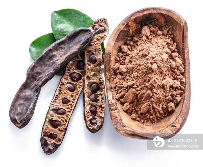 Carob pods and carob powder in the wooden bowl.