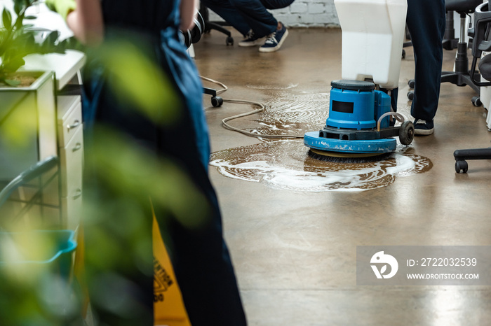 cropped view of cleaner washing floor with cleaning machine near colleagues