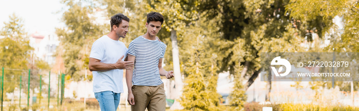 panoramic shot of father walking and talking with teenager son in park